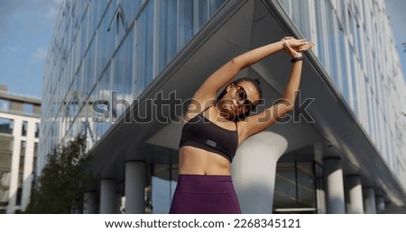 Female runner stretching muscles outdoor at summer morning in city. Healthy young Indian woman warming up outdoors before exercise.