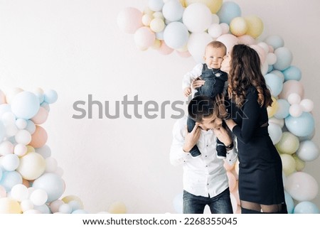Happy family celebrates first birthday of baby boy among a lot of colorful balloons. Celebration first birthday. Festive event. Image with copy space.