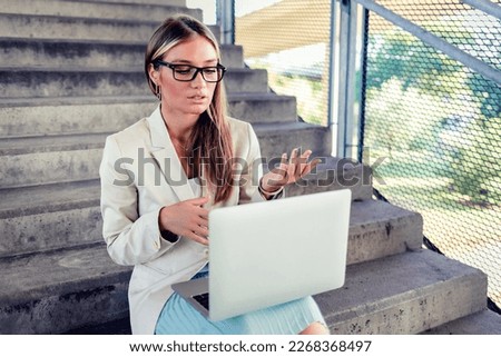 Attractive blond smiling fashionable businesswoman sitting on the stairs outdoors and using laptop. Businesswoman sitting on the steps in a business district working on laptop.