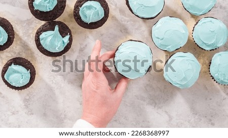 Flat lay. Step by step. Scooping blue buttercream frosting on top of the chocolate cupcakes.
