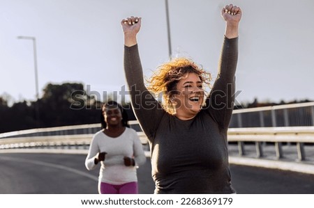 Two excited young plus size women jogging together. Royalty-Free Stock Photo #2268369179