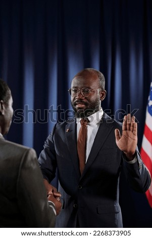 New president of USA with open left palm giving oath of office while looking at mature man and keeping right hand on Holy Bible Royalty-Free Stock Photo #2268373905