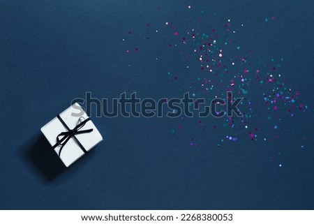 Festive blue background with sparkles and a small white gift box. Happy mother's day, father's day or birthday in dark color scheme. Mockup. copy space