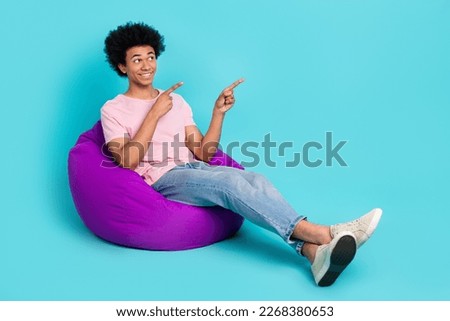 Full body size picture of youngster optimist man sitting soft bean bag direct fingers look empty space brand isolated on cyan color background