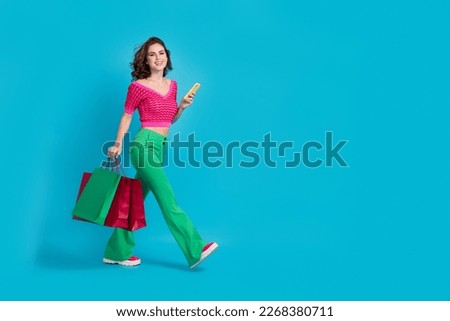 Full length photo of lovely stylish lady wear trendy clothes carry packages walking street go empty space isolated on blue color background