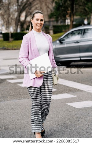 Smiling young caucasian business woman leader entrepreneur, professional manager holding digital tablet computer using software applications standing on the street in big city on sky background