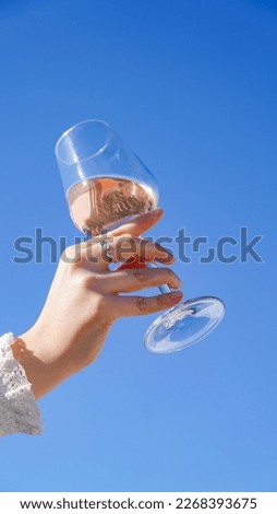 woman hands holding a glass of rosé wine in the air, hand in the blue sky