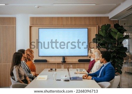 A group of diverse businesspeople are in the meeting room in their company watching a presentation on a led display screen.