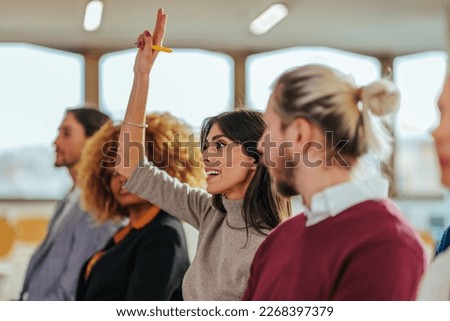 A Caucasian businesswoman is holding her hand up in a conference room to ask the speaker a question. Royalty-Free Stock Photo #2268397379