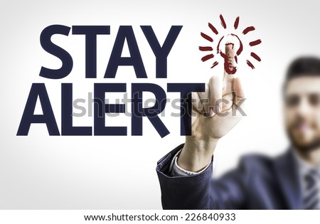Business man pointing to transparent board with text: Stay Alert