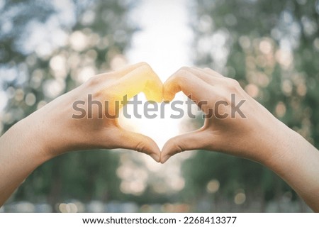 Female hands heart shape on nature green bokeh sun light flare and blur leaf abstract background. Royalty-Free Stock Photo #2268413377
