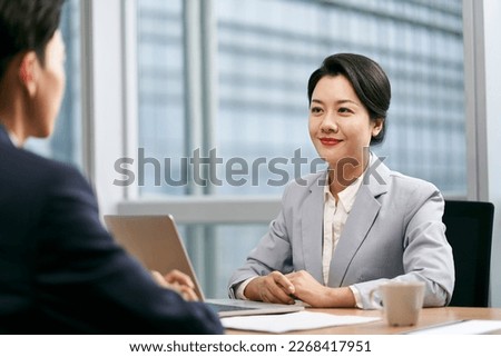 young asian businesswoman female manager sitting at desk talking to male colleague in modern office Royalty-Free Stock Photo #2268417951