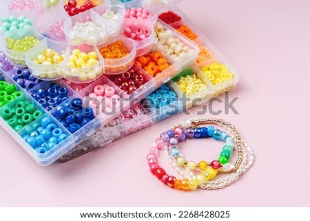 Kids handmade beaded jewelry and different multi-colored beads for children's needlework and crafts in boxes. DIY art activity for kids. Motor skills, creativity and  hobby. Royalty-Free Stock Photo #2268428025