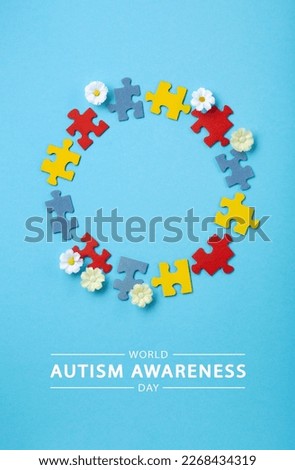 World Autism Awareness Day or month concept. Creative design for April 2. Color puzzle, symbol of awareness for autism spectrum disorder and daisy flowers on blue background. Top view, copy space.