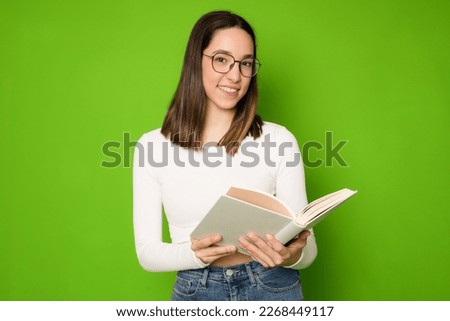 beautiful young woman in glasses with a book in her hands isolated over green background.