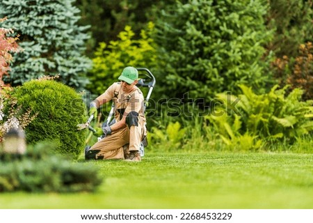 Professional Gardener Shaping Green Shrub with Garden Scissors During Landscape Maintenance Work. Blurred Background with Copy Space. Royalty-Free Stock Photo #2268453229