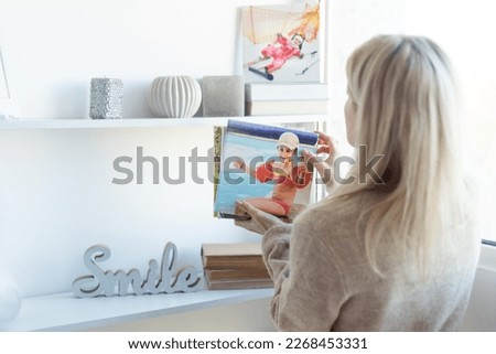Modern Home Interior And Domestic Decor. Smiling young woman hanging painting, putting photo picture frame on the wall. Casual lady taking care of coziness in her new stylish apartment, profile