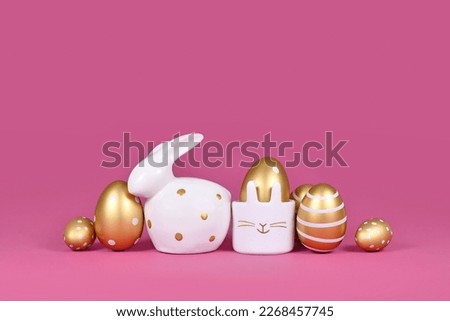 Golden Easter eggs painted with stripes and dots and bunny on pink background with copy space