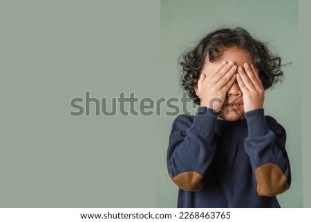 Anxiety - conceptual image of a little boy covering his face with his hands. Scared from something