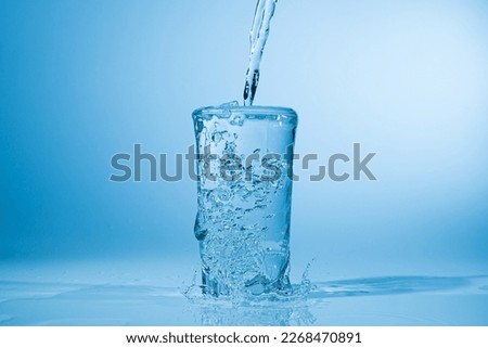 Water pours into a glass on a blue background. Clean drinking water