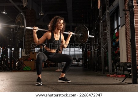 Young pretty african american sports woman in fitness gym lifting up empty bar in gym, doing warm up, barbell squat, butt workout Royalty-Free Stock Photo #2268472947
