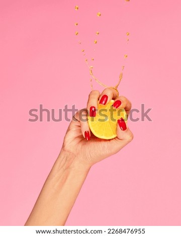 Vitamines. Female hand with bright manicure squeezes half of orange over pink background. Pop art food photography. Drops of juice fly up. Concept of healthy eating, art, fashion, creativity and ad Royalty-Free Stock Photo #2268476955