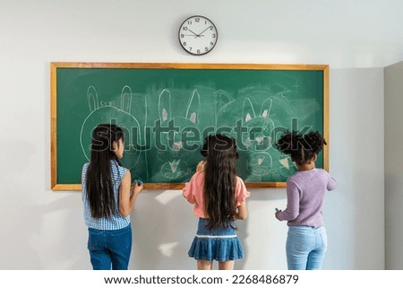Diverse student writing blackboard in classroom at elementary school. Adorable young kids children doing fun activity indoors, drawing cute cartoon on board with happiness together at kindergarten.