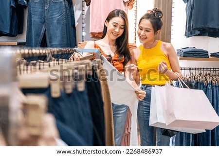Asian two beautiful women looking at clothes product in shopping mall. Attractive happy girl enjoy walking in department store to choose dress and new t-shirt from clothing racks in marketplace center Royalty-Free Stock Photo #2268486937