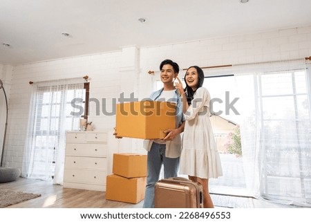 Asian young happy new marriage couple moving to new house together. Attractive romantic man and woman holding box parcel and suitcase with happiness and love. Family-Moving house relocation concept. Royalty-Free Stock Photo #2268496553