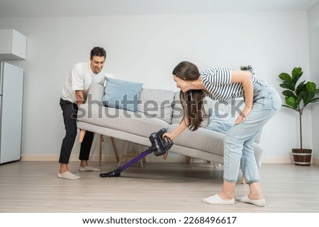 Caucasian young man and woman cleaning living room together at home. Beautiful lovely couple male and female moving sofa and vacuuming messy dirty floor for housekeeping housework and chores in house. Royalty-Free Stock Photo #2268496617