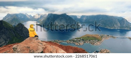 Solitude with nature. Panoramic aerial view of fjord and fishing village. Man tourist sitting on a cliff of rock. Beautiful mountain landscape. Nature Norway, Lofoten islands.  #UniqueSSelf Royalty-Free Stock Photo #2268517061