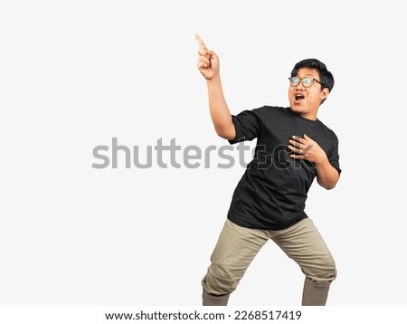 An excited young man looking and pointing to the top of his head with his right hand and suprise expression and the left hand on his chest. A thick guy use eye glasses and black t-shirt pointing  Royalty-Free Stock Photo #2268517419