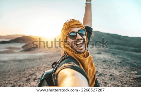 Handsome man taking selfie pic with smart mobile phone outside at golden hour time - Traveler guy with backpack enjoying day out on summer vacation - Happy tourist having fun at summertime holiday Royalty-Free Stock Photo #2268527287