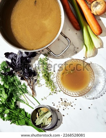 Vegetable stock in glass bowl. Ingredients of stock on the background. Top view