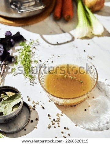 Vegetable stock in glass bowl. Ingredients of stock on the background.