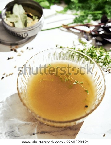 Vegetable stock in glass bowl. Ingredients of stock on the background
