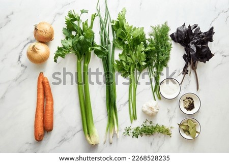Vegetable stock ingredients on white background. Onions and carrots plus greens as green onions, basil and thyme. Leeks and celery