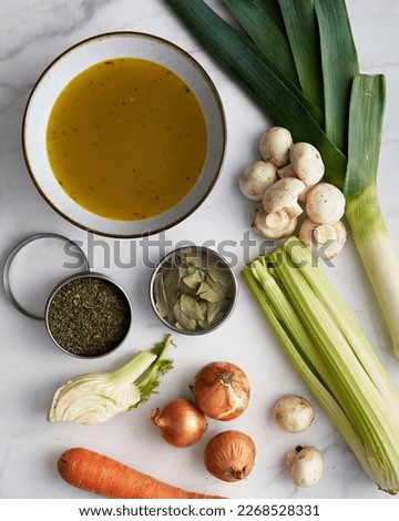 Vegetable stock in a bowl. Ingredients of stock are near: onions and garlic, thyme and leek. Also fennel, carrot and mushrooms. 