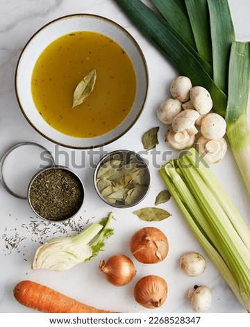 Vegetable stock in a bowl. Ingredients of stock are near: onions and garlic, thyme and leek. Also fennel, carrot and mushrooms. 