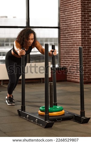 African American athlete is engaged in the gym. A strong woman trains on a crossfit sled. Sport and fitness motivation. Individual sports recreation.