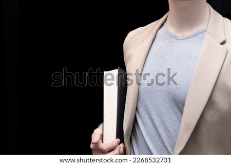a man dressed in smart casual style is holding a thick book. A photo of a student studying