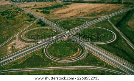 Clover or daisy, simple and cheap type of road junction. Aerial view of beautiful highway road junction in clover shape at summer day. Lorry truck and semi-truck on highway. Car and logistic concept