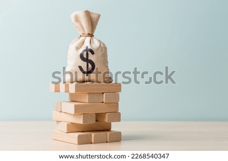 Money bag with Dollar sign on wooden block tower. Business risk and financial instability concept Royalty-Free Stock Photo #2268540347