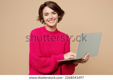Young smiling caucasian cheerful happy smart IT woman wear pink sweater hold use work on laptop pc computer isolated on plain pastel light beige background studio portrait. People lifestyle concept Royalty-Free Stock Photo #2268541497