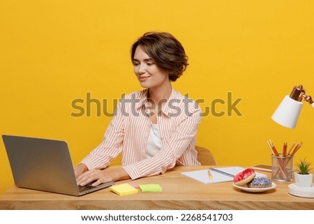 Young happy fun successful employee IT business woman wear casual shirt sit work at office desk using laptop pc computer surfing isolated on plain yellow color background. Achievement career concept