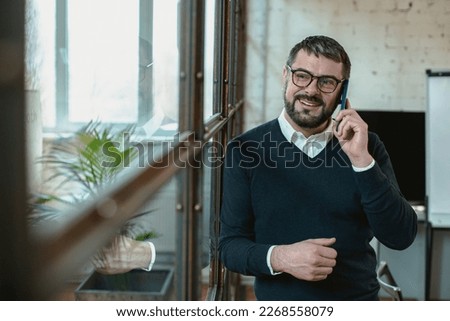 Smiling adult man talking on mobile phone and looking away in the office