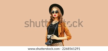 Portrait of stylish young woman photographer with film camera on brown background