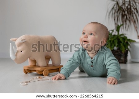 chubby baby in a green jumpsuit is lying on the floor and playing with a wooden toy on a string. High quality photo