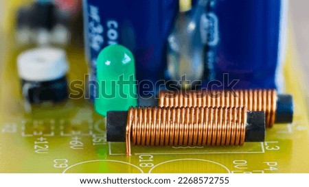 Electromagnetic coils, green LED light and electronic components on printed circuit board. Closeup of cylindric inductors with spiral copper wire on ferrite core or light-emitting diode on yellow PCB. Royalty-Free Stock Photo #2268572755