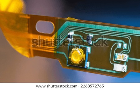 Plastic strip with flexible printed circuit and electronic surface mounted components. Closeup of bent ribbon cable with green and yellow lines of flat PCB dismantled from headphones. E-waste recycle. Royalty-Free Stock Photo #2268572765